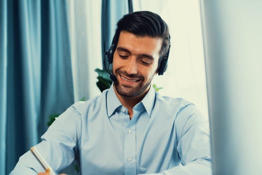 Male call center operator or telesales representative siting at his office desk wearing headset and engaged in conversation with client providing customer service support or making a sale. fervent