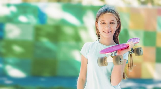 Portrait of smiling teenage girl holding pink skateboard in park and looking at the camera