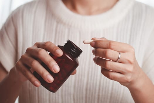 Asian woman's hand pouring medicines from a brown bottle for healthcare concept.