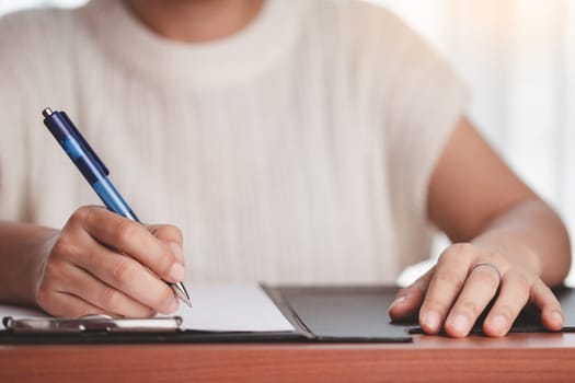 Asian woman's hand holding a pen and writing something on the notebook for the concept of work and study.