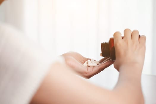 Asian woman's hand pouring medicines from a brown bottle for healthcare concept.