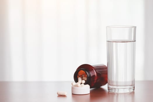 A glass of drinking water with piles of tablets were released from the brown bottle on the table for healthcare concept.