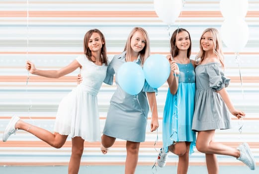 Beautiful girls in dresses holding balloons on striped background