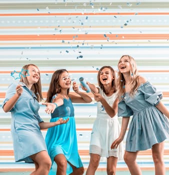 Smiling girls shoot confetti on striped background