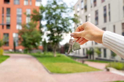 Hand holding keys on the background of a new building, construction concept. Buying real estate, housing, apartments. Private yard, park, kindergarten, playgrounds