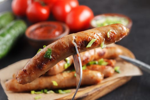 sausage on a fork on the background of sausages with vegetables and various sauces on the table.