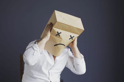 Sad man with a bag on his head, with a drawn crying emoticon.
