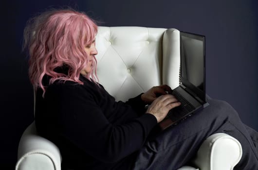 A man in a pink wig sits in a white chair and works at a computer.