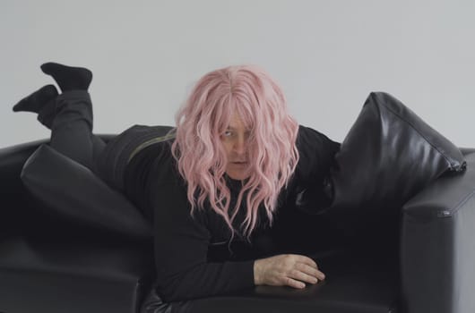 A drunk man in a pink wig lies on the couch, wakes up, raises his head and straightens his hair.