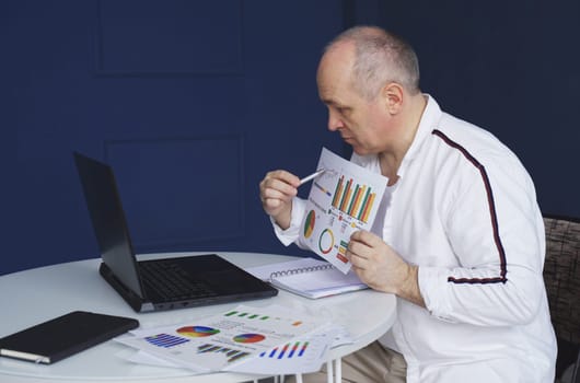 A man makes an online video call chat, sitting at home and talking into a laptop webcam, showing a document.