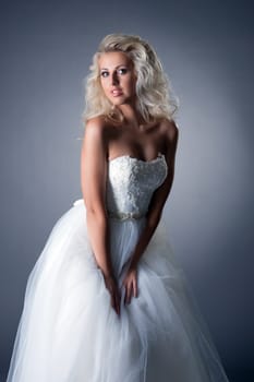 Romantic blonde posing in lush wedding dress, on gray background