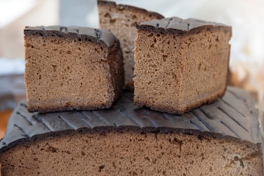 A loaf of black rye bread on the counter of a bakery is cut into pieces, close-up.Texture of black ecological bread