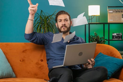 Stressed lebanese man at home room looking at unpaid bank debt bills, doing paperwork, planning budget, calculate finances mortgage payments. Arabian guy throws paper bills sitting on couch. Lifestyle