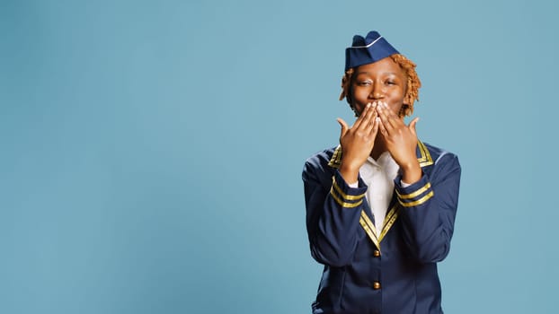 Female aircrew member sending air kisses on camera, acting flirty and cute in studio. Young stewaress dressed in uniform showing romantic sweet gesture, doing kissy face. Aviation job.