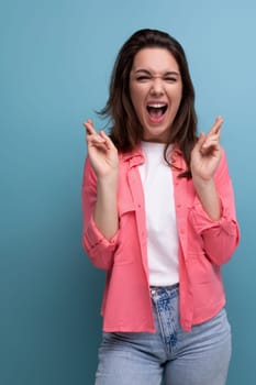 portrait of optimistic brunette young woman in shirt and jeans with fingers crossed in hope.