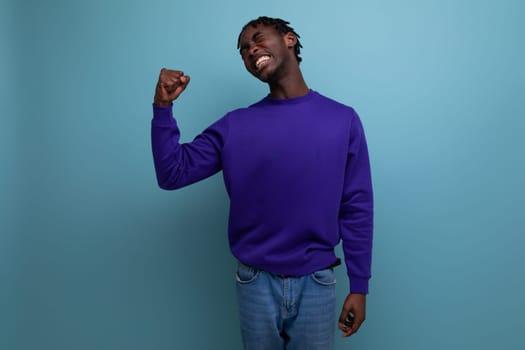 dark-skinned young brunette man with dreadlocks in a blue sweatshirt shows muscles.