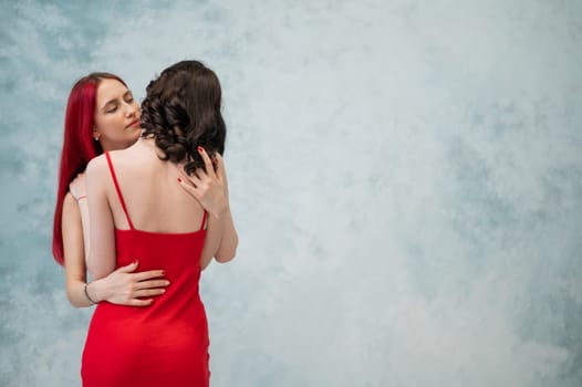 A close-up portrait of two tenderly embracing women dressed in identical red dresses. Lesbian intimacy