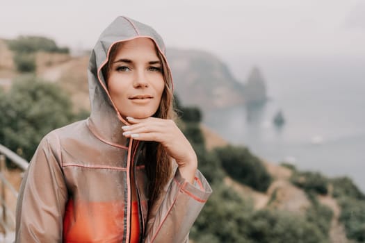 Woman rain park. Happy woman portrait wearing a raincoat with transparent umbrella outdoors on rainy day in park near sea. Girl on the nature on rainy overcast day