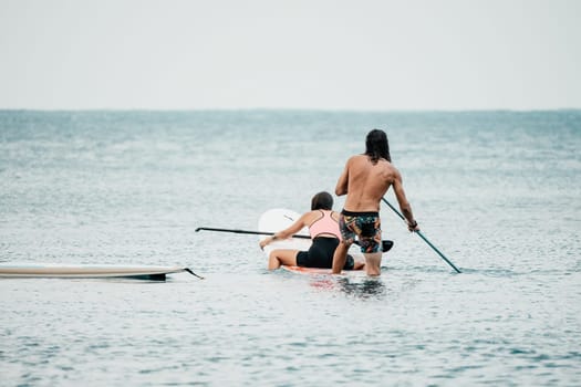 Sea woman and man on sup. Silhouette of happy young woman and man, surfing on SUP board, confident paddling through water surface. Idyllic sunset. Active lifestyle at sea or river