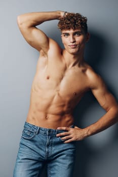 man bicep smile gray jeans shirtless standing young fitness studio handsome background fashion fit curly guy