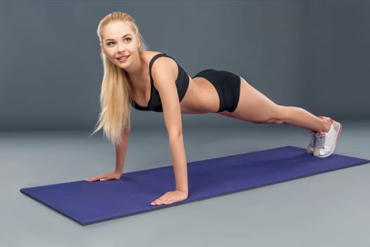 Young beautiful woman in fitness wear trained female body, doing push-ups on the mat