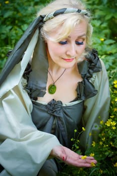 Adult mature woman 40-60 in a green long fairy dress in forest. Photo shoot in style of dryad and queen of nature. Fairy in beautiful green summer forest. Concept of caring for nature