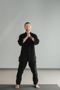 A man in black kimano practicing qigong energy exercises indoors.