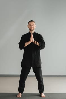 A man in black kimano practicing qigong energy exercises indoors.