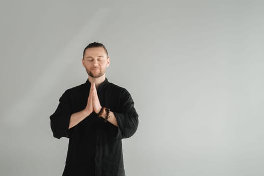 A man in black kimano practicing qigong energy exercises indoors.