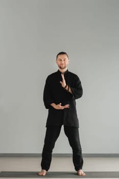 A man in black kimano practicing qigong energy exercises indoors.