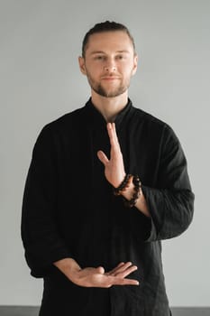 A man in black kimano practicing qigong energy exercises indoors.