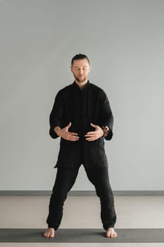 A man in black kimano practicing qigong energy exercises indoors.