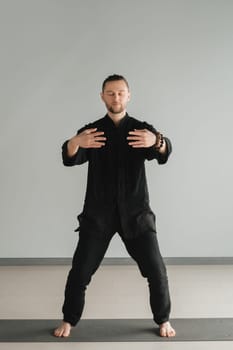 A man in black kimano practicing qigong energy exercises indoors.