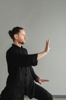 A man in black kimano practicing qigong energy exercises indoors.