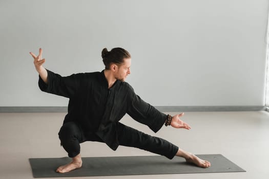 A man in black kimano practicing qigong energy exercises indoors.