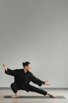 A man in black kimano practicing qigong energy exercises indoors.