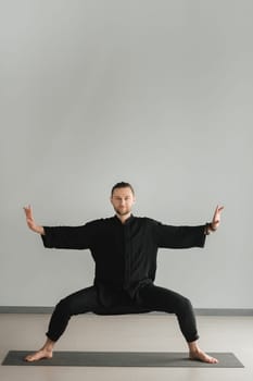 A man in black kimano practicing qigong energy exercises indoors.