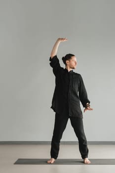 A man in black kimano practicing qigong energy exercises indoors.