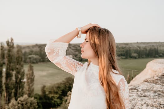 Romantic beautiful bride in white dress posing with sea and mountains in background. Stylish bride standing back on beautiful landscape of sea and mountains on sunset