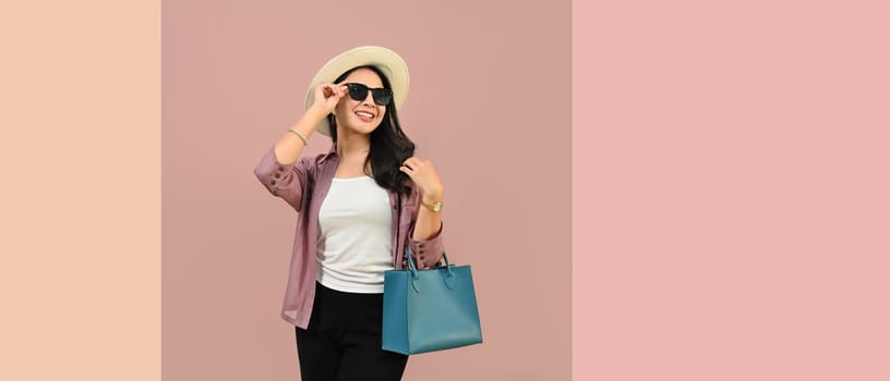 Portrait of cheerful young woman wearing summer clothes and sunglasses isolated on pink background with copy space.