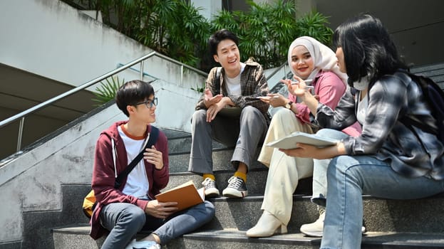 Group of university students sitting on stairs and talking to each other after classes. Education and youth lifestyle concept.