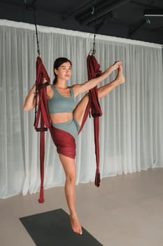 A girl does yoga in a hanging hammock in the gym. Fly yoga in the gym.