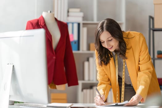 Young attractive female fashion designer sketching idea on paper at desk, working with a laptop at home.