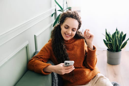 Happy lady browsing e-commerce sites or watching funny videos on a smartphone. Enjoying online leisure A smiling young woman uses a cell phone for online shopping or entertainment at home on the couch