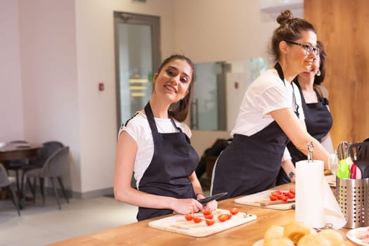 Cooking course, chef in cook uniform teaches young people cooking class students to prepare and mix ingredients for dishes in restaurant kitchen