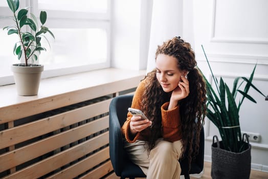 Relaxed woman browsing modern apps and texting messages on smartphone at home. Happy lady using mobile phone for internet browsing and online shopping. Mobile phone user messaging, shopping from home.