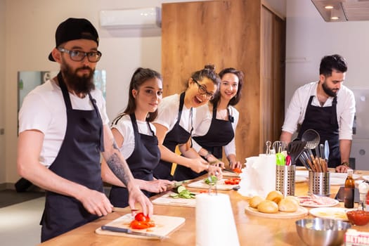 Cooking course concept - senior male chef in cook uniform teaches young people cooking class students to prepare and mix ingredients for dishes in restaurant kitchen