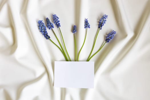 Top view of blank white greeting card Mum flowers on white folded fabric. Mothers day, wedding concept