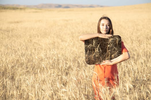 Young woman in the wheat field, holding mirror glass where reflected the dry grass. Meditation, mental health concept. Copy space