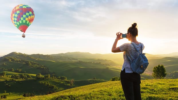 Woman taking photo of balloon on mobile phone at the mountain peak.